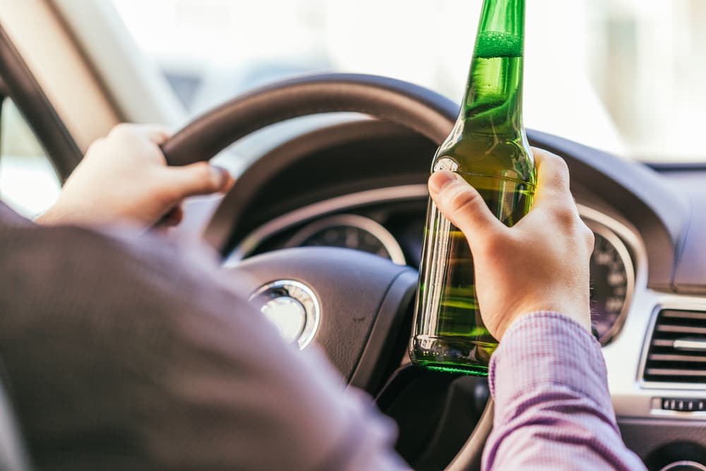 Man drinking alcohol while driving a car, illustrating the dangerous behavior of driving under the influence.