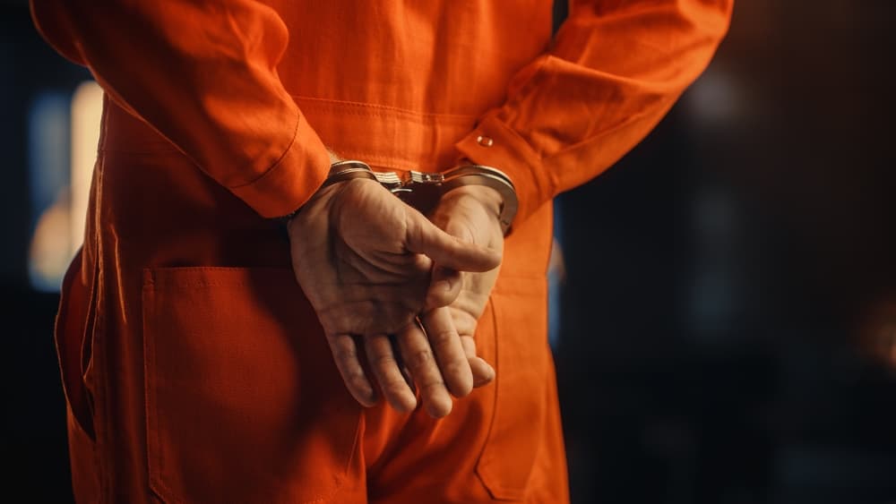 Close-up of a handcuffed convict in an orange jumpsuit during a court trial, symbolizing the legal process and sentencing of a criminal.